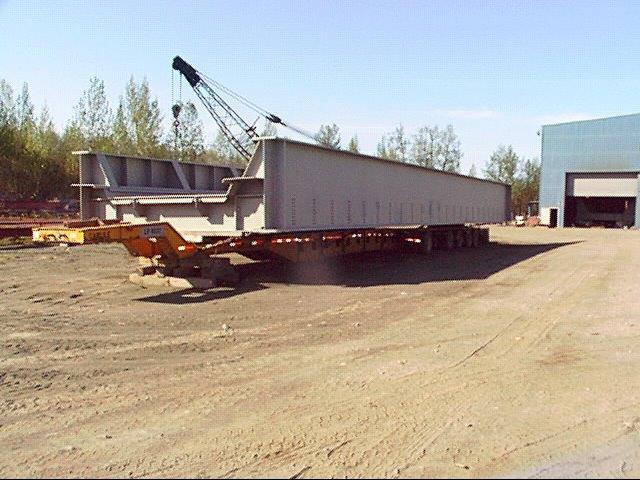 Section of gray railroad bridge staged on a trailer, outside of facility
